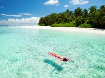 Serena fuga tropicale: un momento di relax mentre una persona galleggia senza sforzo nelle acque cristalline del Mare Estero, con rigogliose palme e l'orizzonte infinito oltre.