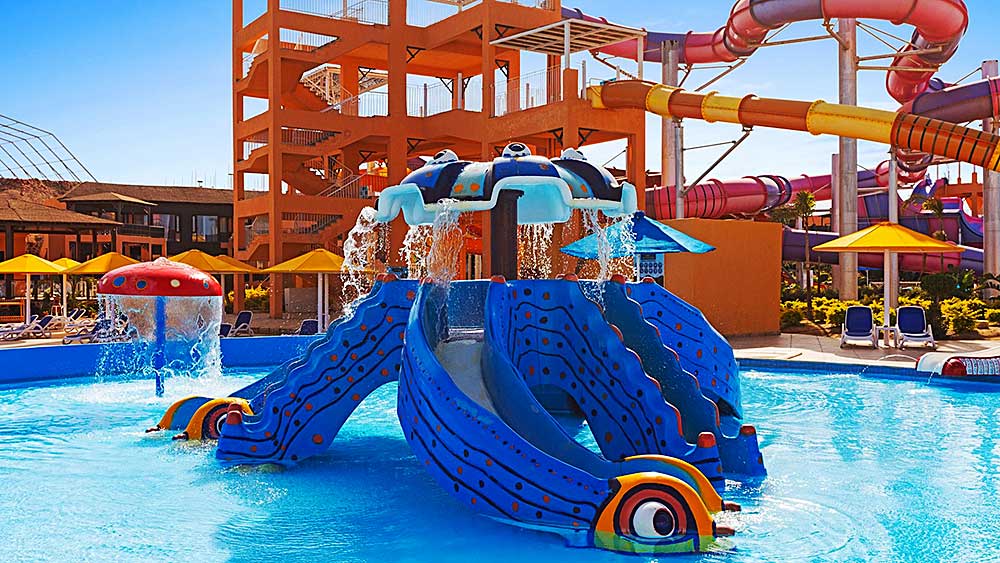 Colorata area giochi acquatica per bambini con scivoli e irrigatori nel soleggiato parco acquatico all'aperto del Villaggio Mar Rosso.