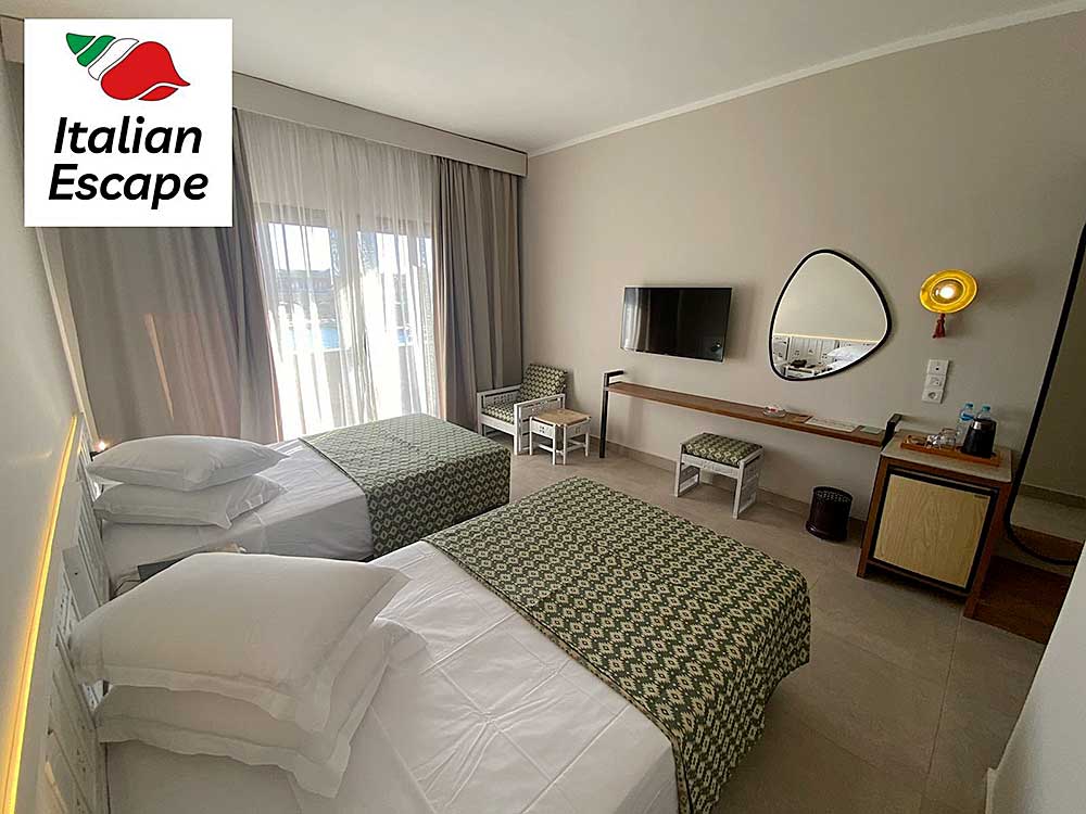 Una ordinata camera d'albergo con letti gemelli, caratterizzata da arredi moderni e decorazioni a tema italiano, fa parte del villaggio Sharm El Sheikh offerto da SBS Viaggi.