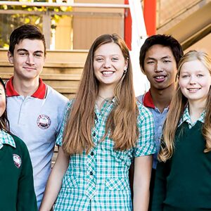 Un gruppo di sette studenti liceali sorridenti, alcuni con maglioni verdi e altri con polo grigie, in piedi all'aperto vicino alle scale.