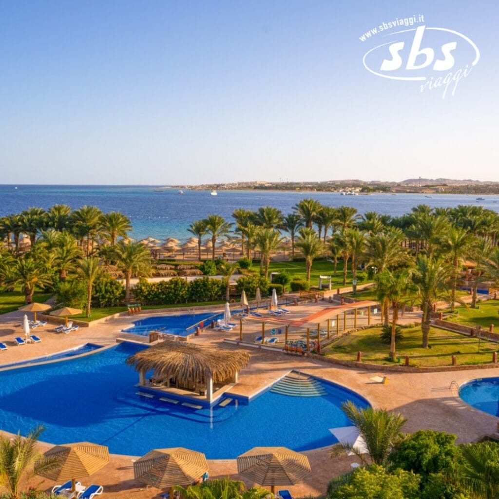 Vista aerea del Fort Arabesque Resort, un paradiso costiero con palme, ville lussuose e una grande piscina con una capanna dal tetto di paglia. Ombrelloni e sedie a sdraio punteggiano il paesaggio, con l'oceano sereno sullo sfondo: il relax completo vi attende in questa squisita destinazione spa.