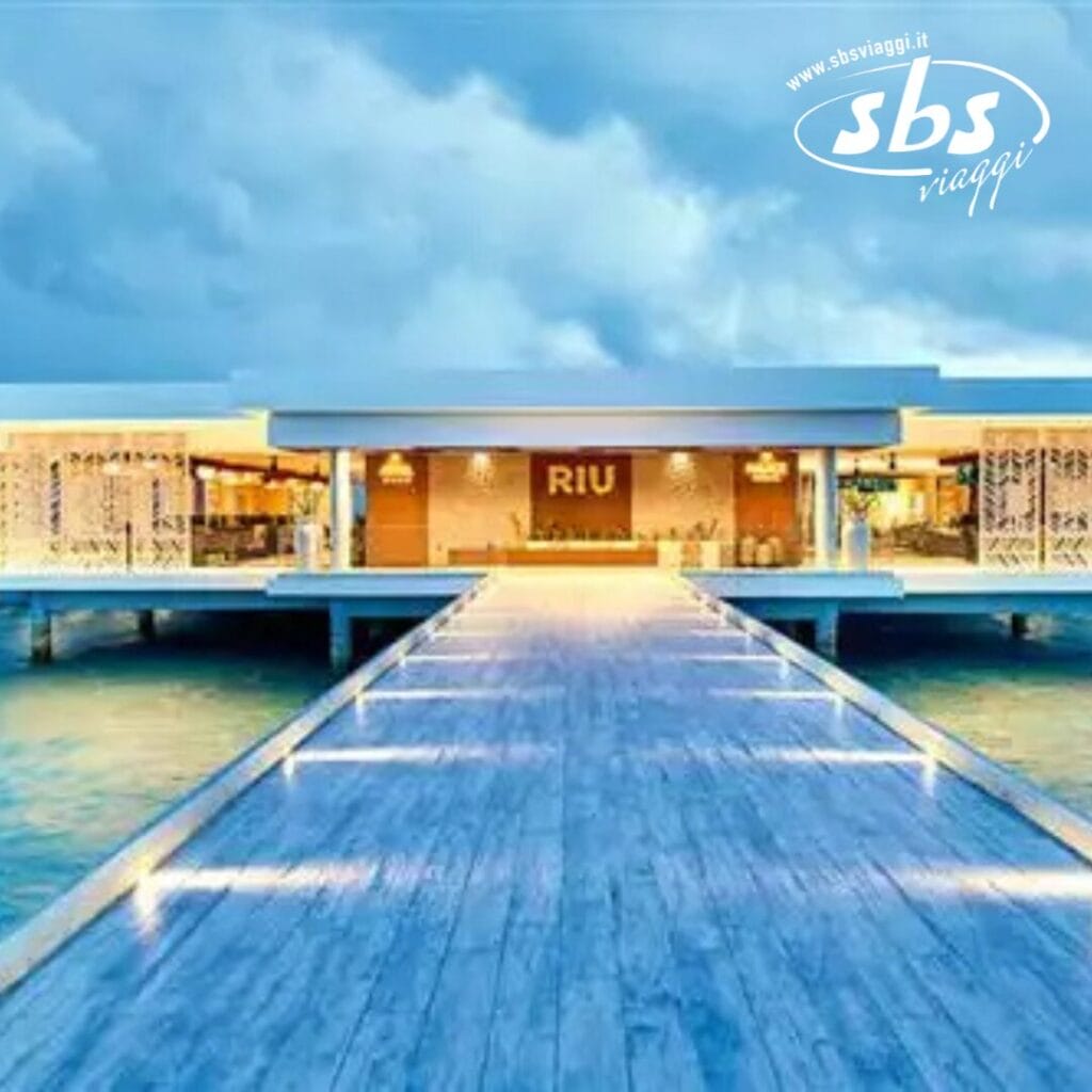 Un molo moderno si estende con eleganza sulle acque calme, conducendo all'edificio RIU, adagiato sotto un cielo nuvoloso nella serena bellezza delle Maldive.