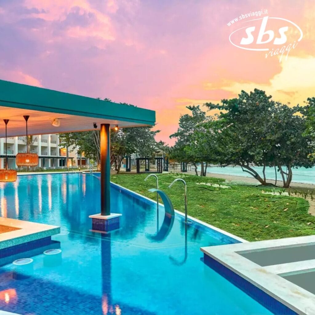 Provate la serenità di una piscina a sfioro con bar sull'acqua che si affaccia sull'oceano al tramonto, circondata da alberi rigogliosi e da una vivace area verde.