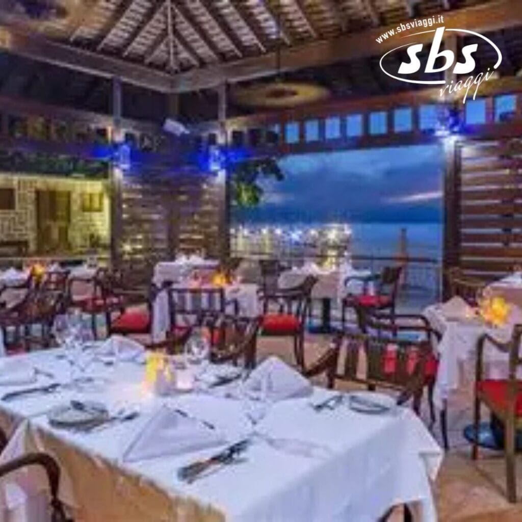 Al Royal Decameron Montego Beach, goditi un ristorante all'aperto con tavoli ordinatamente apparecchiati che si affacciano sul lungomare al tramonto. L'arredamento in legno e l'illuminazione calda creano un'atmosfera accogliente, perfetta per gli ospiti di età superiore ai 16 anni. Il logo