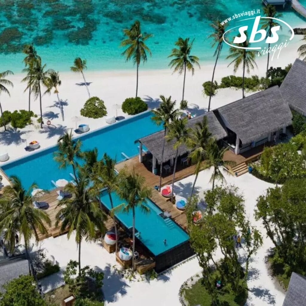 Vista aerea del Cora Cora Maldives, un resort tropicale con due piscine rettangolari, palme rigogliose e una spiaggia di sabbia bianca adiacente all'oceano turchese.