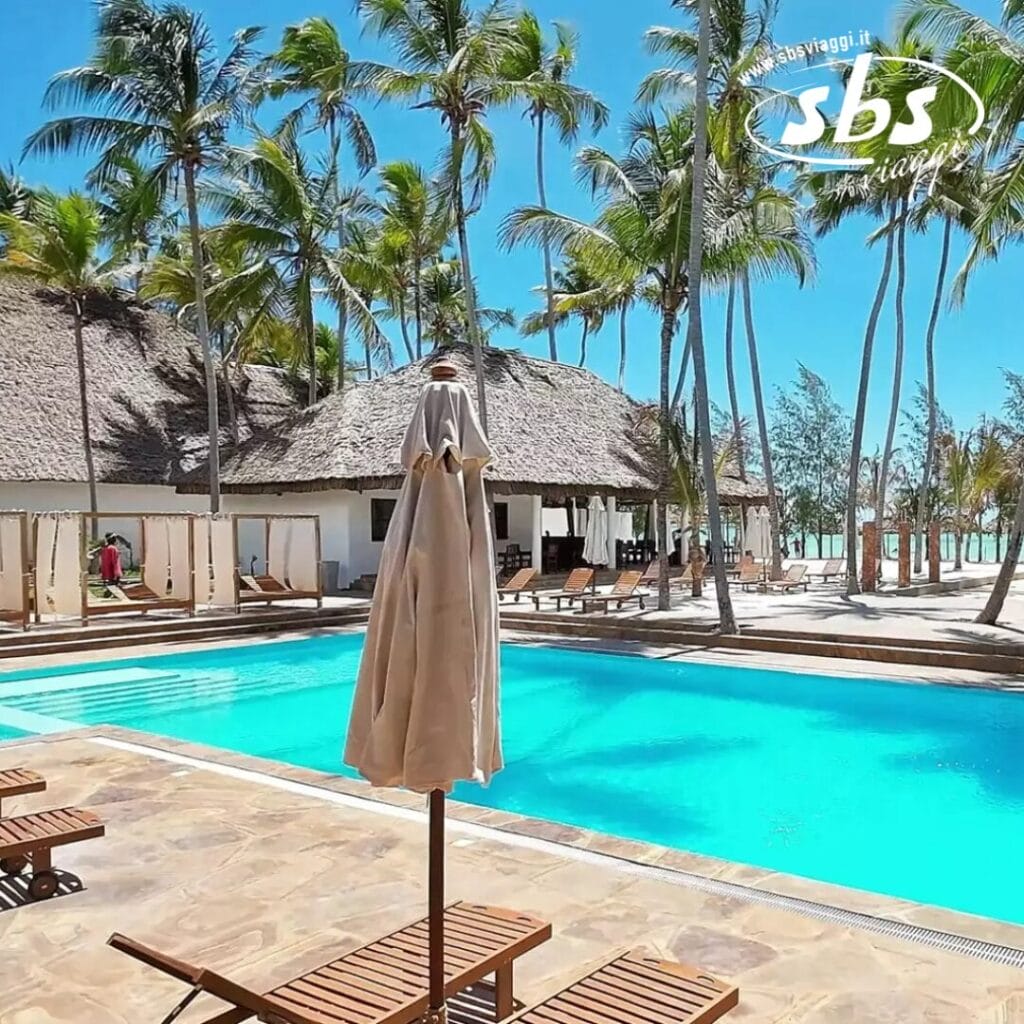 L'area piscina dello Zanzibar Resort è caratterizzata da palme, sedie a sdraio e graziosi edifici con tetti di paglia, il tutto sotto un limpido cielo azzurro.
