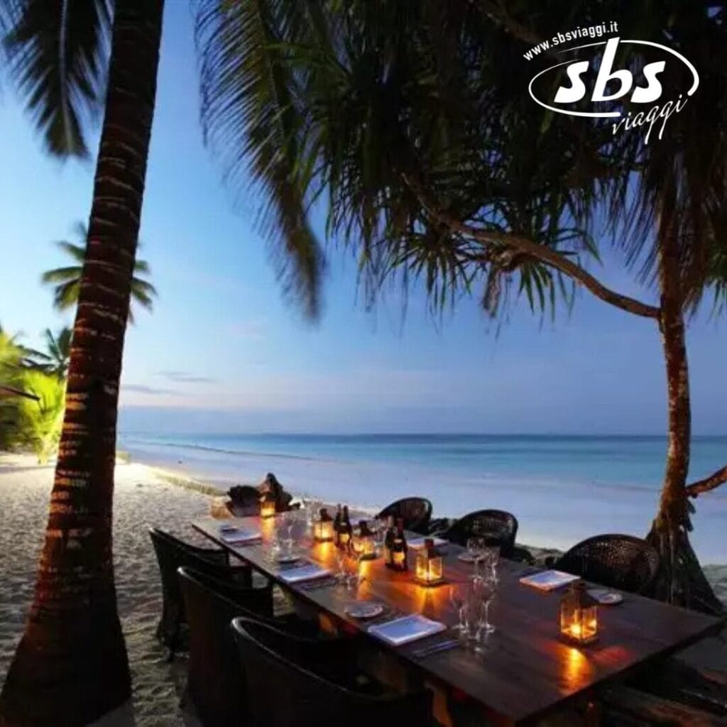 Una cena in riva al mare, con un tavolo di legno illuminato da candele e decorato con bicchieri e bottiglie, offre una scena pittoresca sotto le palme al tramonto: una perfetta bozza automatica.