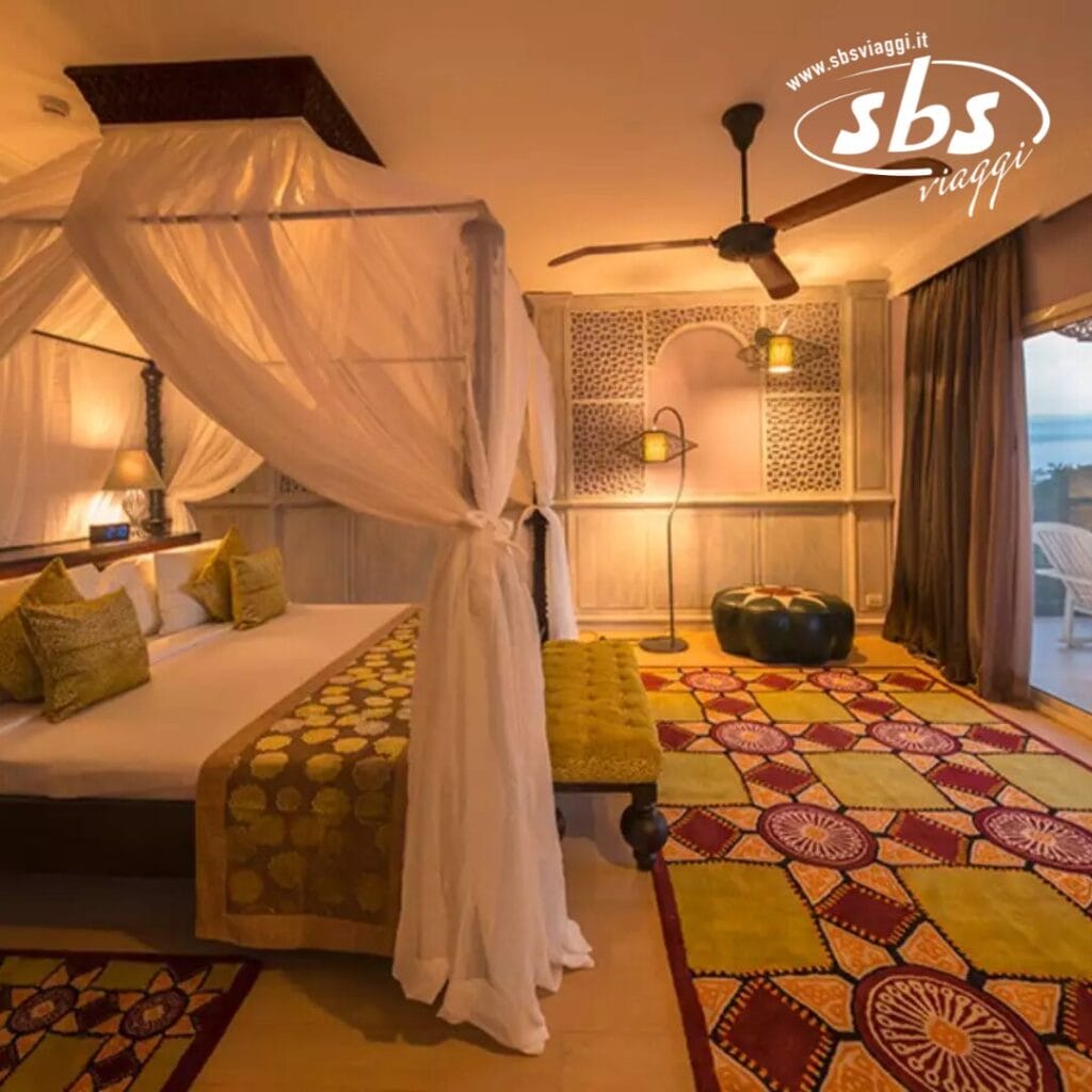 Un'accogliente camera d'albergo al Riu Palace Zanzibar è dotata di un letto a baldacchino, tappeti colorati e una vista sul balcone. La camera dello Zanzibar Hotel è decorata con luci calde e cuscini decorativi per un soggiorno invitante.