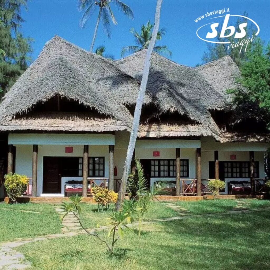 Edificio con tetto di paglia, colonne di legno e un prato curato, circondato da alberi e piante tropicali. Un logo nell'angolo recita
