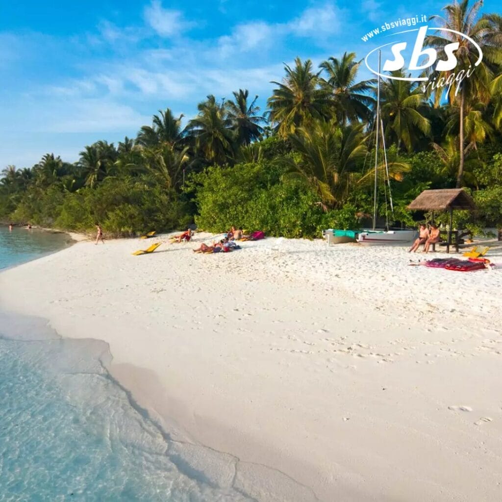 Scena di spiaggia tropicale con persone che si rilassano sulla sabbia bianca dell'isola di Embudu vicino all'acqua limpida, circondate da palme e vegetazione lussureggiante. Una piccola struttura con tetto di paglia, tipica del fascino pittoresco che si trova in un resort sull'isola, è visibile sullo sfondo.