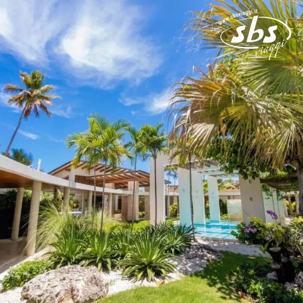 Un lussureggiante giardino tropicale con palme e un cielo azzurro terso circonda un moderno padiglione all'aperto e un'area piscina, creando l'oasi perfetta per un resort sulla spiaggia di Punta Cana. Godetevi l'atmosfera serena arricchita da un'invitante esperienza spa.