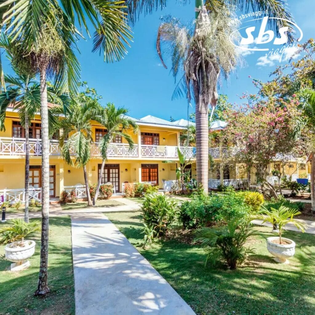Il Merril's Beach Resort vanta un cortile tropicale adornato da palme, incastonato in un edificio giallo a due piani e sotto un limpido cielo azzurro.