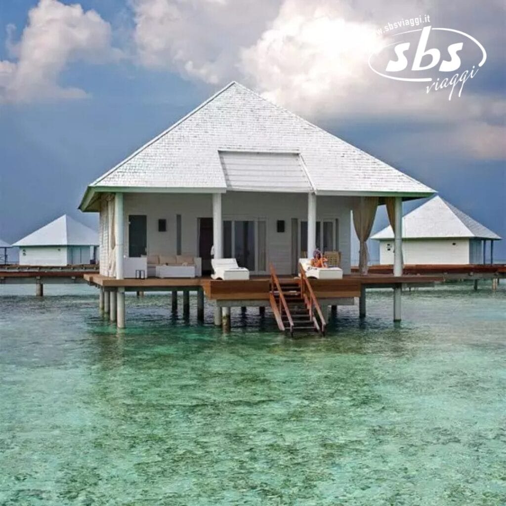 Scopri la bellezza serena della nostra Water Villa, che ricorda lo stile Seaclub, appollaiata con grazia su palafitte. Questo bungalow sull'acqua con il suo immacolato tetto bianco è avvolto dalle acque cristalline e turchesi di Athuruga Beach sotto un cielo parzialmente nuvoloso.