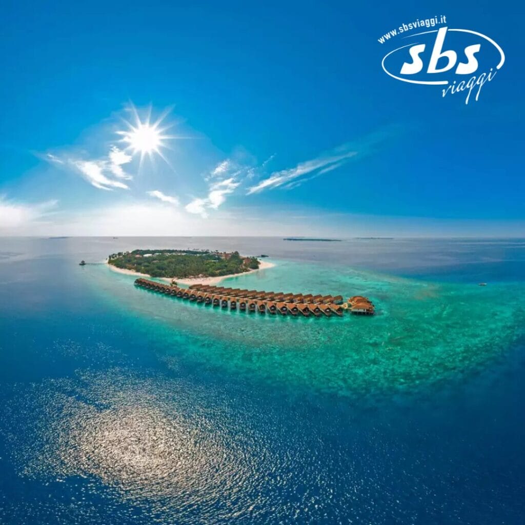 Vista aerea dell'isola del Reethi Faru Resort con bungalow sull'acqua circondati dall'oceano turchese sotto un cielo limpido.