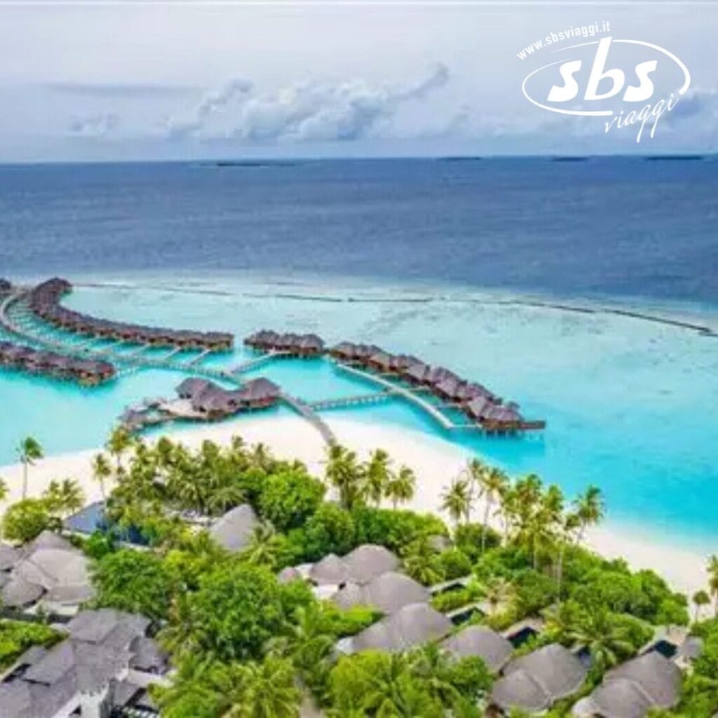 Vista aerea di un resort tropicale alle Maldive, con bungalow sull'acqua al Sun Siyam Iru Fushi, circondati da un oceano azzurro e cristallino e da una spiaggia sabbiosa fiancheggiata da palme.