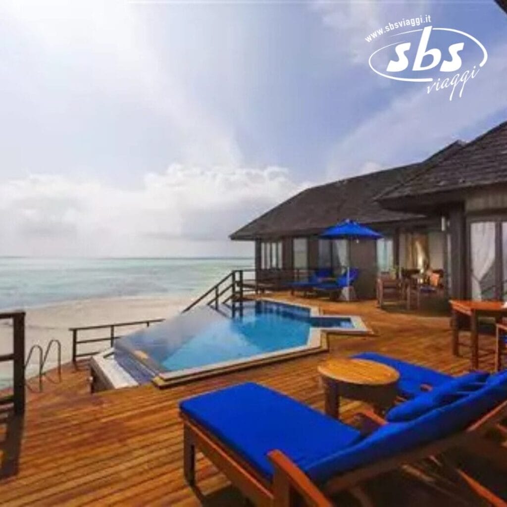 Villa fronte oceano con bozza automatica, sedie a sdraio, un tavolo, una piscina e una vista sul mare. Una struttura coperta abbellisce lo sfondo mentre il cielo è parzialmente nuvoloso.