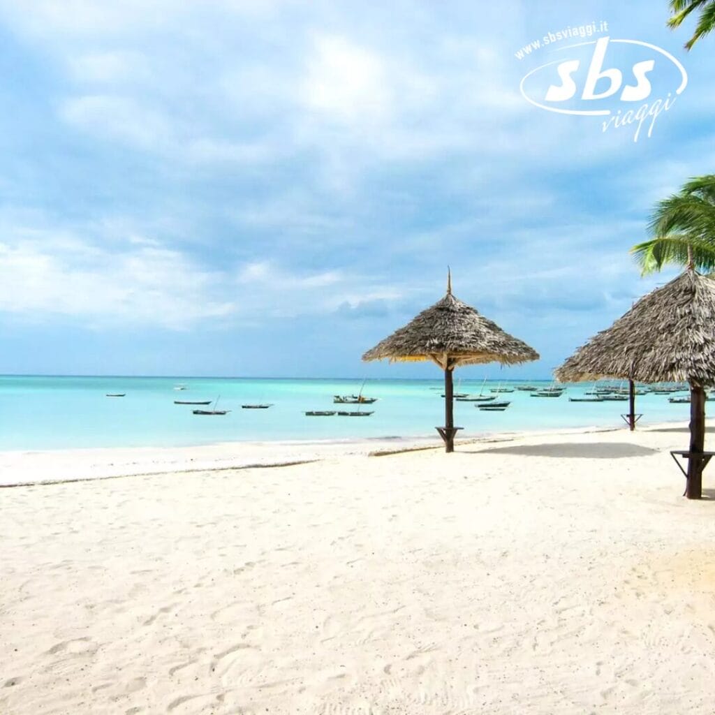 La scena della spiaggia tropicale è caratterizzata da sabbia bianca e acqua turchese sotto un cielo nuvoloso, con barche di legno che ondeggiano dolcemente. Nelle vicinanze, due ombrelloni di paglia offrono ombra a coloro che assaporano il perfetto mix di bellezza naturale e bozza automatica.