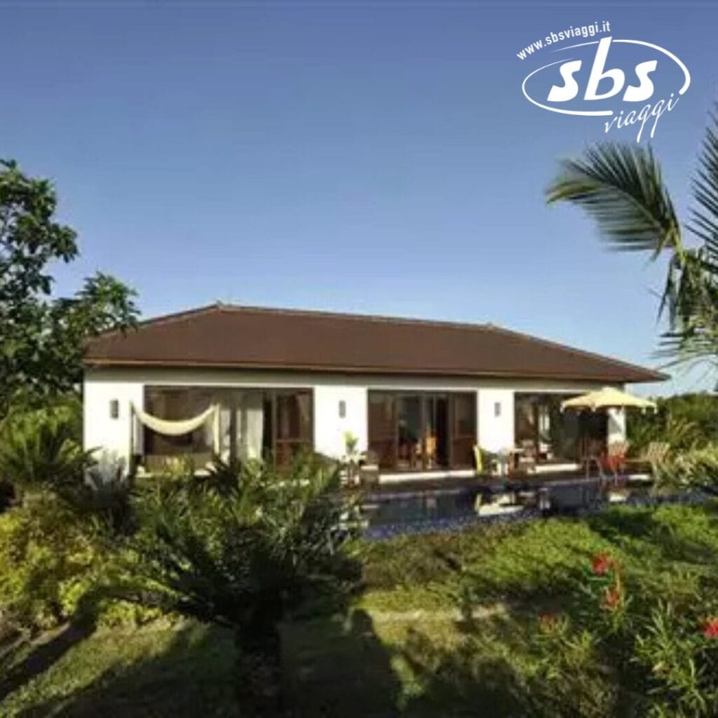 Una villa tropicale in un resort di lusso, circondata da una vegetazione lussureggiante con una piccola piscina e un ponte di fronte. Questo rifugio sull'isola incarna tranquillità ed eleganza. L'immagine presenta il logo