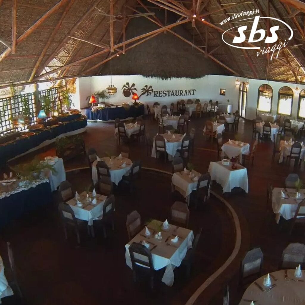 Un ristorante con tetto di paglia, pavimento in legno e tavoli coperti da tovaglie bianche crea l'atmosfera ideale per la cena, fondendo armoniosamente tradizione e stile in un tripudio di eleganza culinaria.