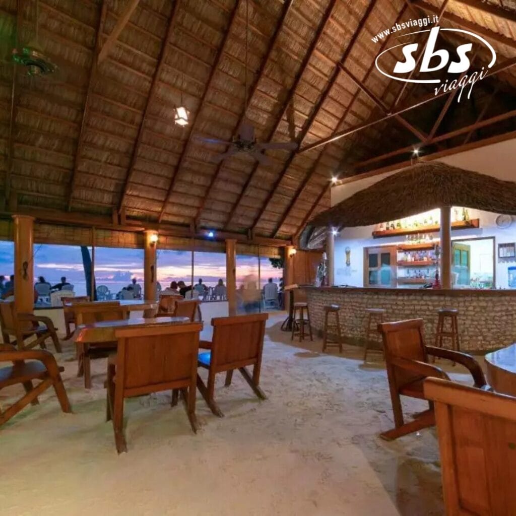 Bar sulla spiaggia con mobili in legno, tetto di paglia e una vista aperta sull'oceano al tramonto, che ricorda il fascino tropicale di Fihalhohi.