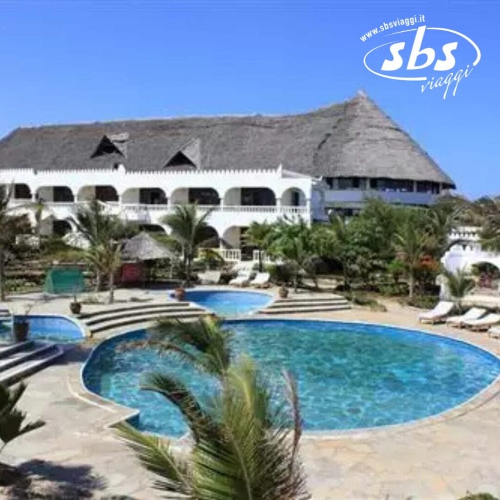 Il Jumbo Watamu offre un rifugio sereno con la sua ampia piscina, circondata da rigogliose palme e invitanti lettini prendisole, il tutto sullo sfondo affascinante di un edificio con tetto di paglia.