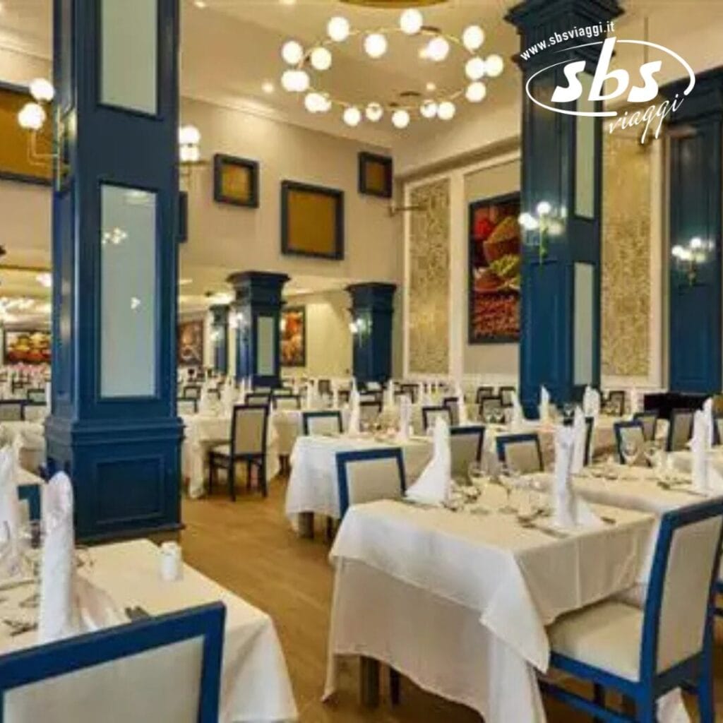 Gli spaziosi interni del ristorante Riu Palace di Punta Cana sono caratterizzati da colonne blu, tovaglie bianche, apparecchiature ordinate e un'illuminazione elegante, che creano un'atmosfera raffinata e invitante.