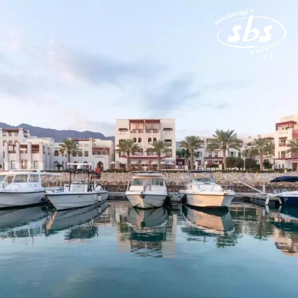 Le barche attraccano in un tranquillo porto turistico di fronte al Sifawy Boutique Hotel, con le palme che ondeggiano dolcemente e le montagne che si stagliano contro il cielo limpido sopra di loro.