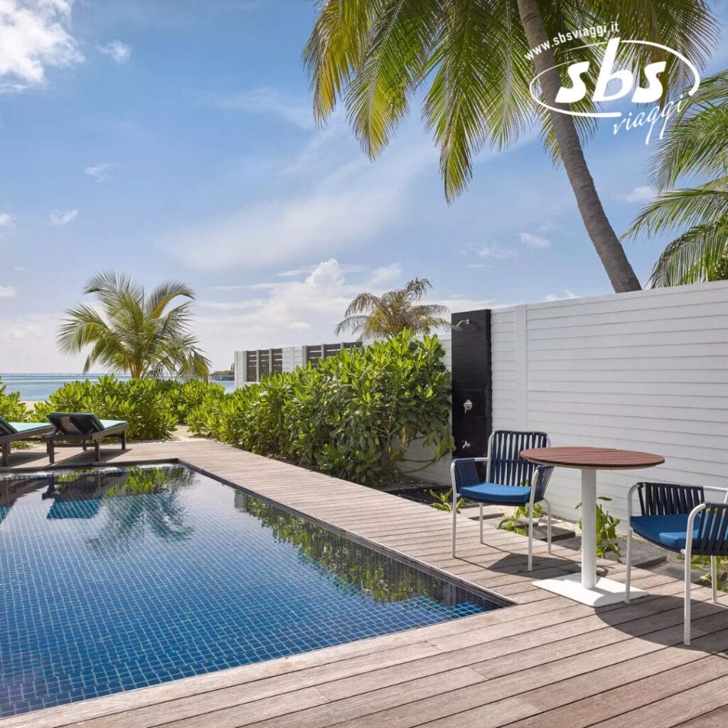 L'ambiente tropicale all'aperto è caratterizzato da una piscina circondata da sedie a sdraio e un tavolo, il tutto immerso tra le palme sotto un cielo limpido: una rilassante esplosione di paradiso.