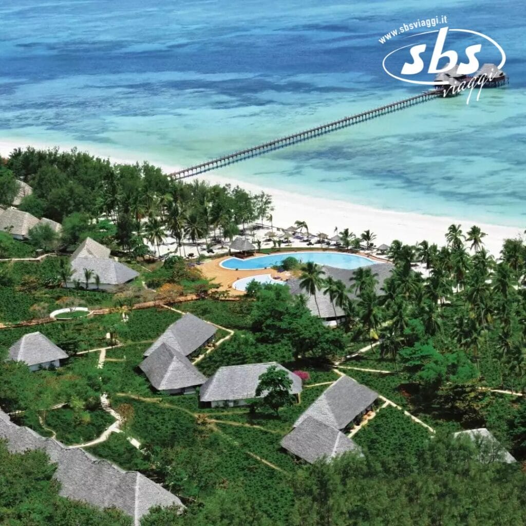Vista aerea del resort tropicale di Dongwe con ville con tetti di paglia, vegetazione circostante, una piscina, palme e un lungo molo di legno che si estende nel mare turchese.