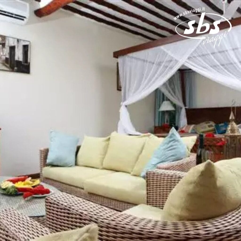 Accogliente soggiorno con mobili in vimini, cuscini giallo chiaro e un letto a baldacchino sullo sfondo. Un logo