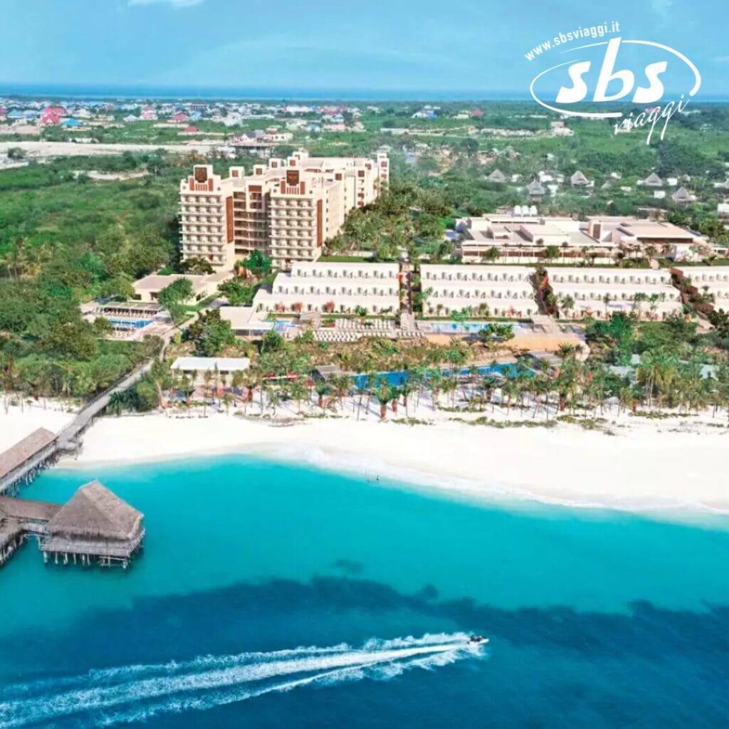Vista aerea del Riu Jambo Hotel, un resort sulla spiaggia con paesaggi tropicali, una spiaggia di sabbia bianca e un motoscafo che scivola tra le acque turchesi.