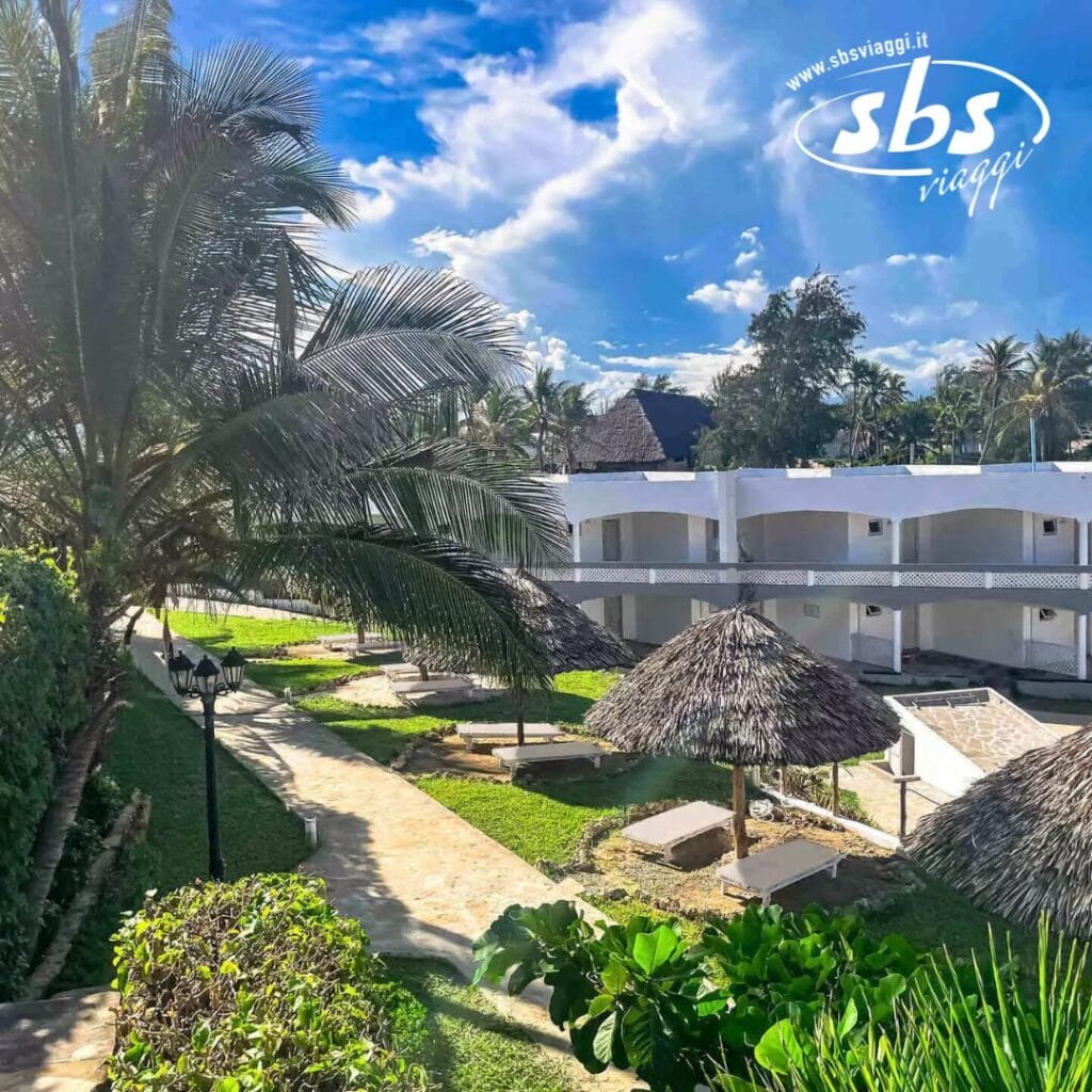 Vista di un resort tropicale con palme, edifici bianchi e strutture con tetti di paglia sotto un cielo azzurro e terso: uno scenario di bozza automatica in cui la natura incontra il fascino architettonico.