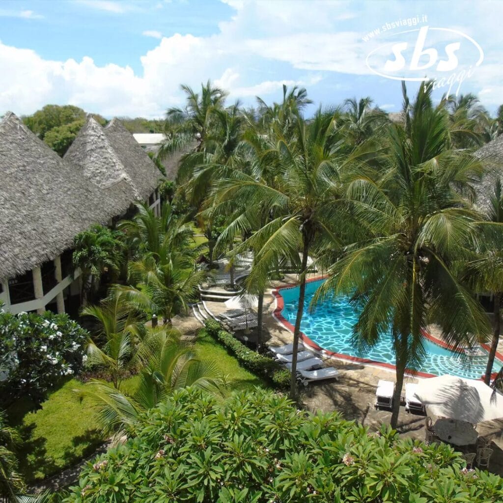 Un lussureggiante resort tropicale, l'Aquarius Club, è caratterizzato da palme, edifici con tetti di paglia e una piscina circondata da sedie a sdraio sotto un cielo azzurro.