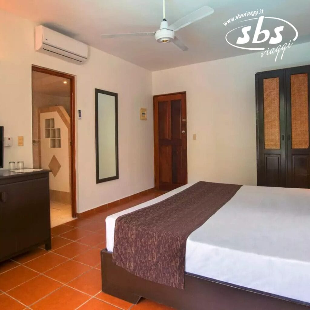 Vivi un soggiorno accogliente al Whala! Bavaro in una camera dotata di un comodo letto, eleganti mobili marroni, ventilatore a soffitto e aria condizionata efficiente. Un piccolo ingresso conduce al bagno. Le pareti sono di un bianco immacolato e il pavimento piastrellato aggiunge un tocco di fascino classico.