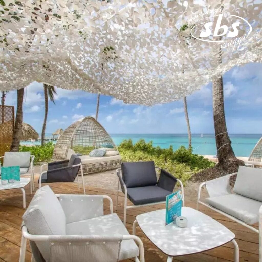 L'area lounge sulla spiaggia del Catalonia Royal La Romana è dotata di sedie in vimini, divani e un baldacchino. Con vista sull'oceano e palme ondeggianti sullo sfondo, questo posto tranquillo è riservato esclusivamente agli ospiti di età superiore ai 18 anni che cercano una fuga tranquilla.