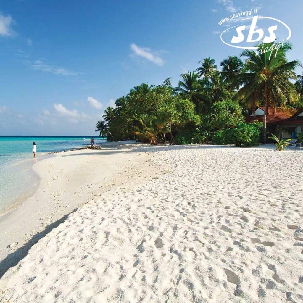 Athuruga Beach offre una vista mozzafiato con le sue rive sabbiose, l'acqua azzurra e cristallina e le palme verdi e rigogliose sotto un cielo parzialmente nuvoloso; una persona si ferma vicino al bordo dell'acqua, forse ammirando la vicina Water Villa in vero stile Seaclub.