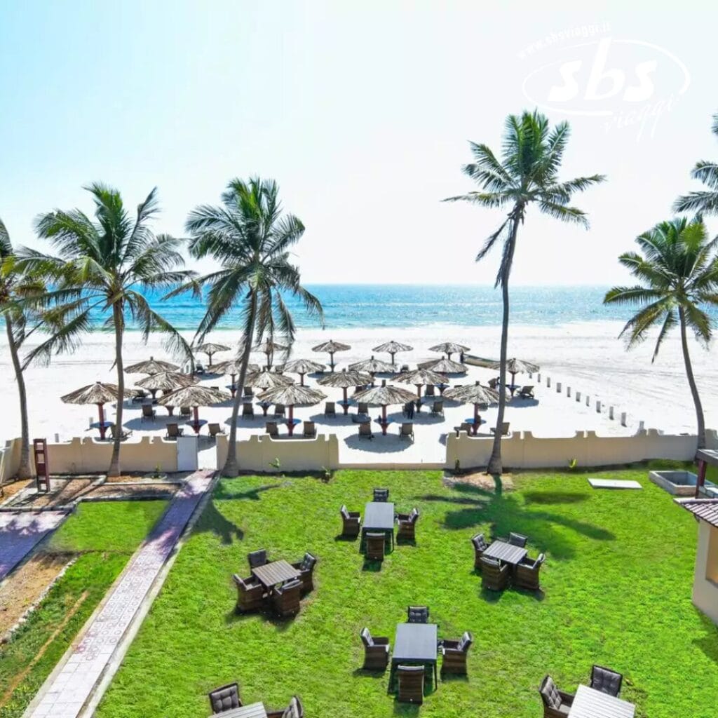 Godetevi una vista sulla spiaggia con palme e lettini prendisole adagiati sotto gli ombrelloni. Una bozza automatica rivela un'area erbosa con tavoli e sedie, perfetta per il relax. L'oceano luccica sullo sfondo sotto un cielo limpido, creando la scena per una fuga idilliaca.