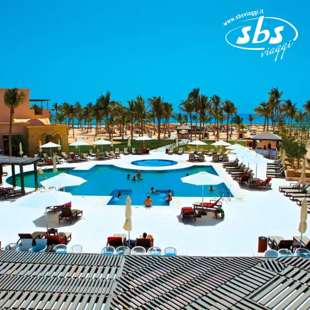 L'area piscina del resort, completa di lettini e ombrelloni Bozza automatica, è circondata da graziose palme. Gli ospiti nuotano e si rilassano mentre lo sfondo della spiaggia e dell'oceano incontra un cielo azzurro e limpido.