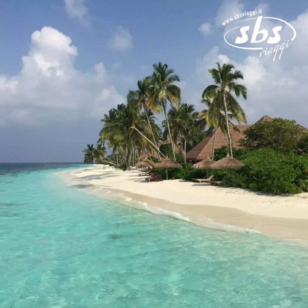 Il Reethi Faru Resort offre una splendida spiaggia tropicale fiancheggiata da palme e ombrelloni di paglia, il tutto sullo sfondo di acque turchesi e cristalline e di un cielo azzurro brillante.