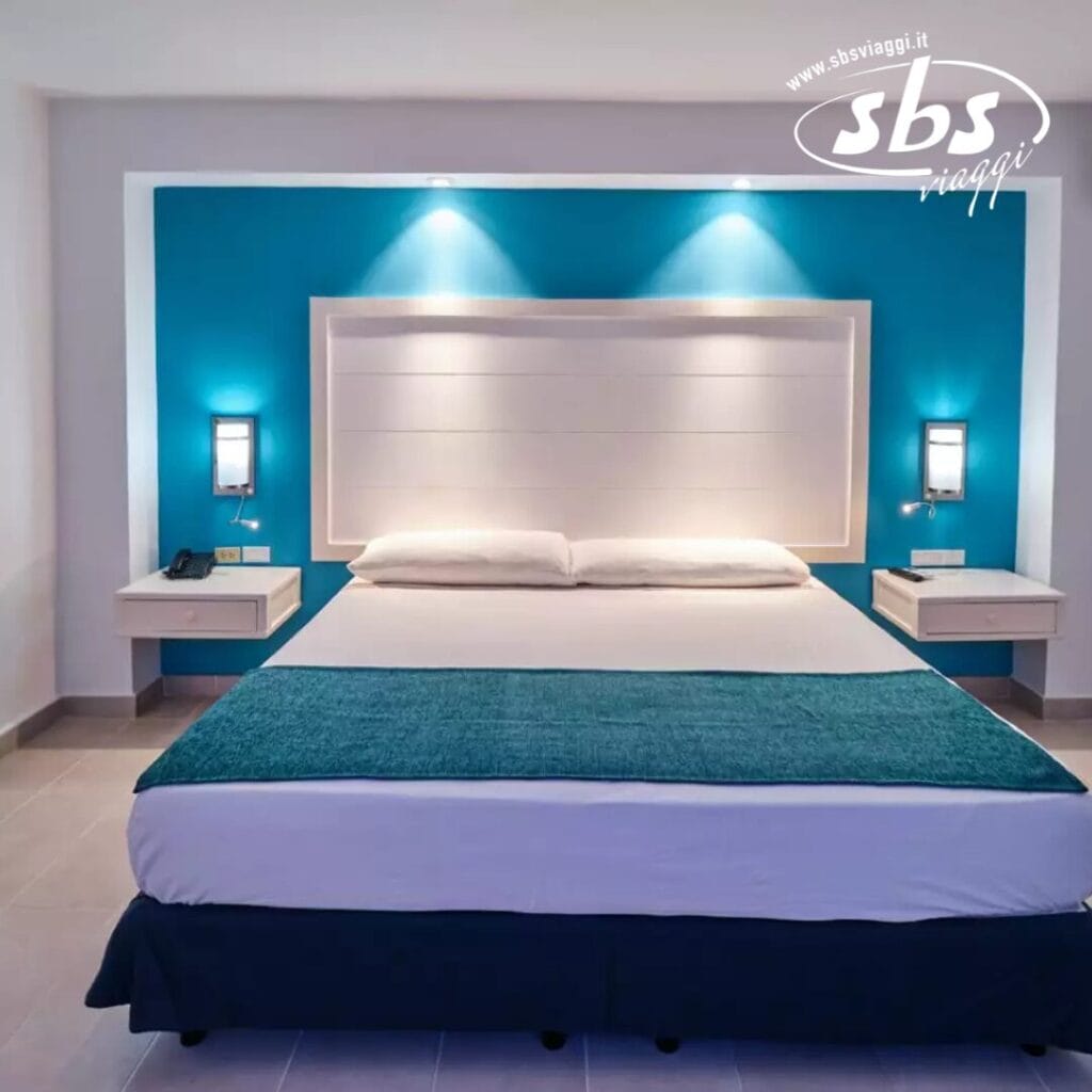 Una moderna camera d'albergo presenta un letto matrimoniale con lenzuola bianche e verde acqua, comodini sospesi e lampade a parete su una splendida parete decorativa verde acqua, abbracciando un tocco di eleganza bozza automatica.