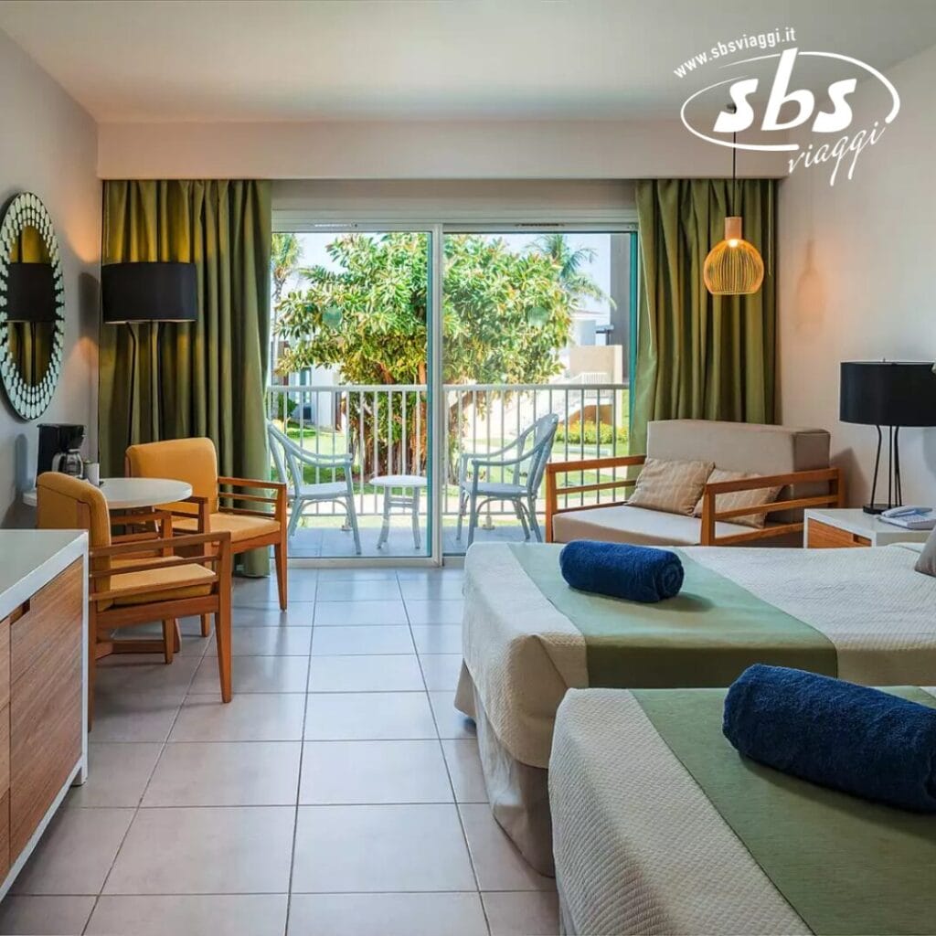 Provate una moderna camera d'albergo con due letti e accenti verdi. Rilassatevi nell'accogliente area soggiorno mentre vi godete la vista sul giardino attraverso le porte scorrevoli in vetro. Il logo nell'angolo in alto mostra con orgoglio