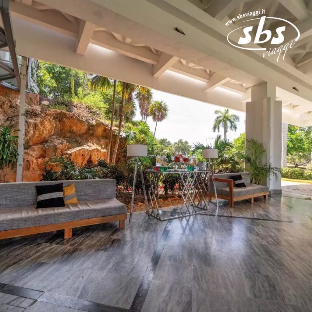 L'accogliente area salotto esterna coperta del Veraclub è dotata di due divani grigi e un tavolo di metallo con bevande. La vegetazione lussureggiante e le rocce offrono uno sfondo tranquillo, che ricorda le spiagge tranquille di Varadero.