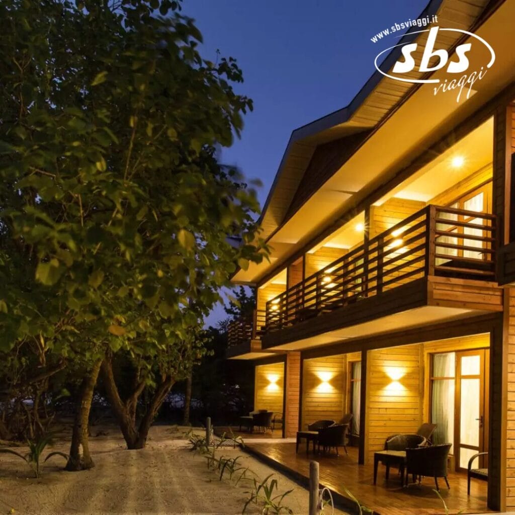 Immerso tra alberi sussurranti, il resort boutique a due piani risplende al tramonto. I balconi illuminati si affacciano sul sentiero sabbioso, offrendo una fuga serena al Pearl Sands Hotel.