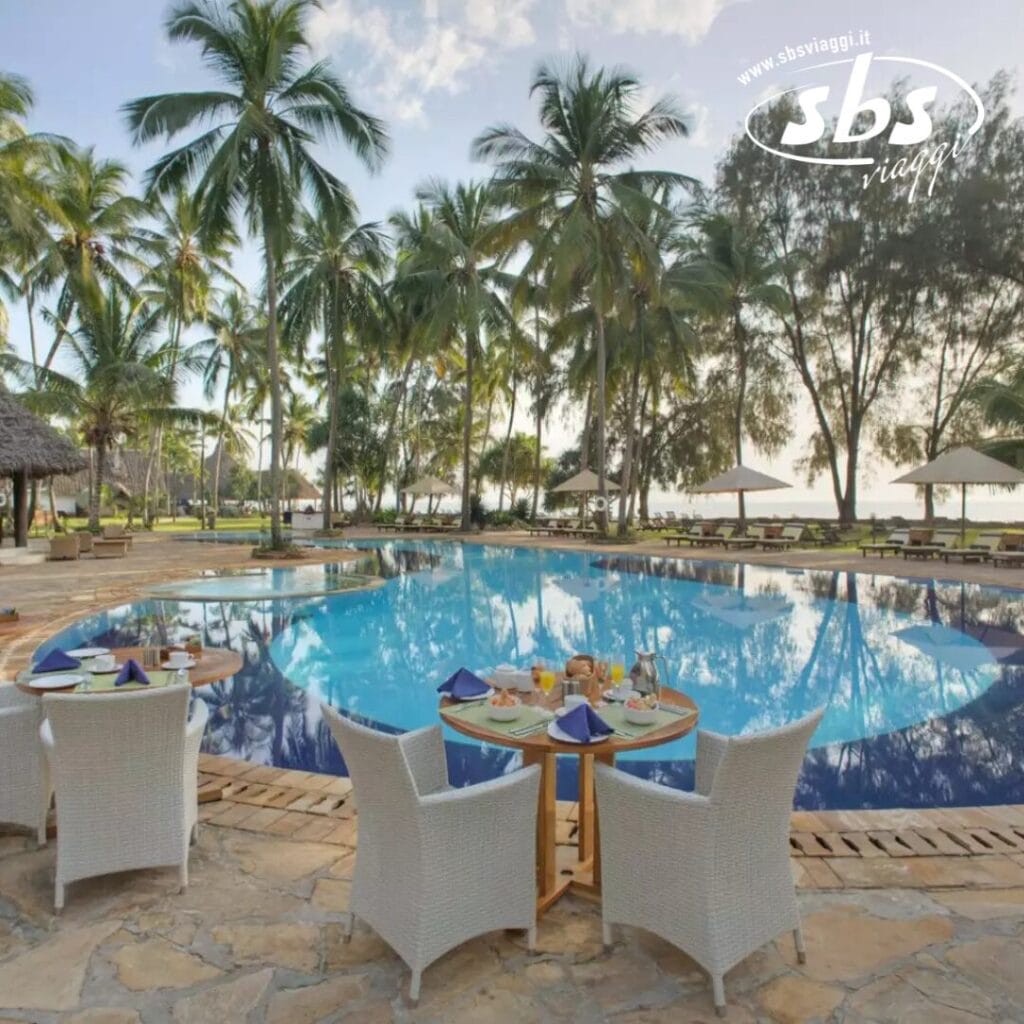 Vista a bordo piscina con palme e l'oceano sullo sfondo. Quattro sedie e un tavolo apparecchiato per la colazione sono in primo piano, catturando l'atmosfera serena del Bluebay Beach Resort.