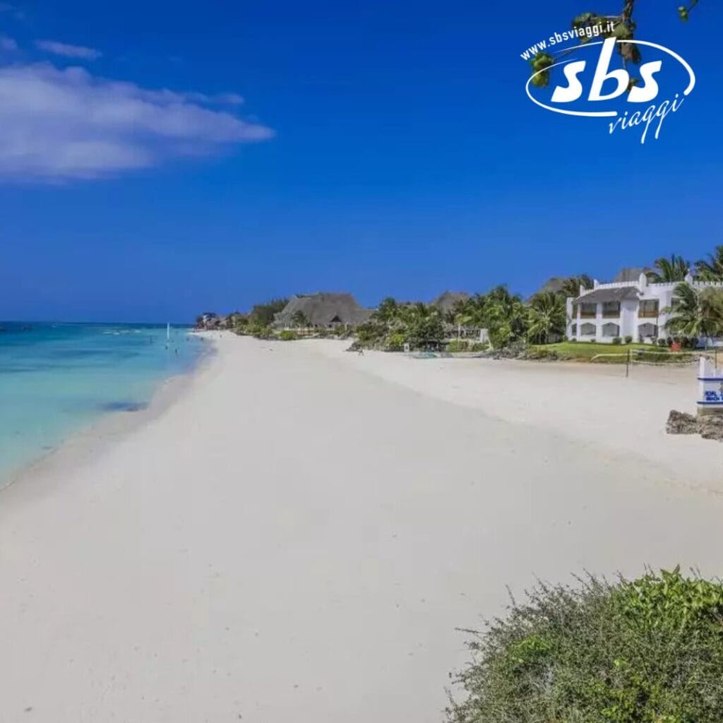 Uno scenario sereno sulla spiaggia del Royal Zanzibar Beach Resort, con sabbia bianca, acqua cristallina, palme ondeggianti e incantevoli edifici sulla spiaggia sotto un cielo perlopiù limpido.