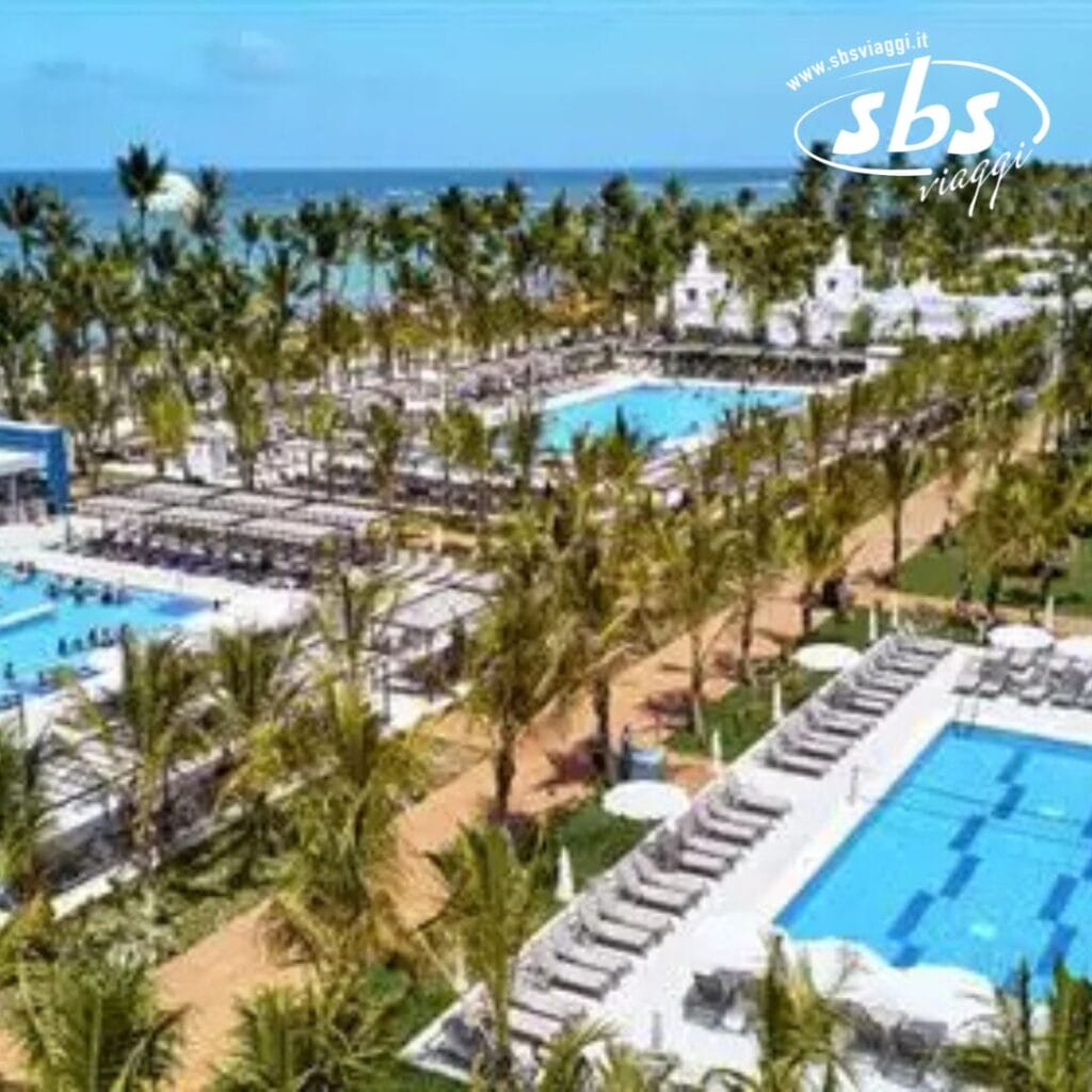 Il resort sulla spiaggia Riu Palace Punta Cana vanta numerose piscine, circondate da palme e sedie a sdraio, con una vista mozzafiato sull'oceano sullo sfondo.