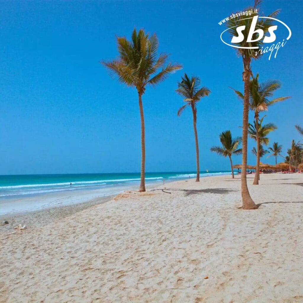 Le palme ondeggiano dolcemente su una spiaggia sabbiosa sotto un cielo azzurro e limpido, con le onde turchesi dell'oceano che si infrangono sullo sfondo: un'esplosione di perfezione della natura.