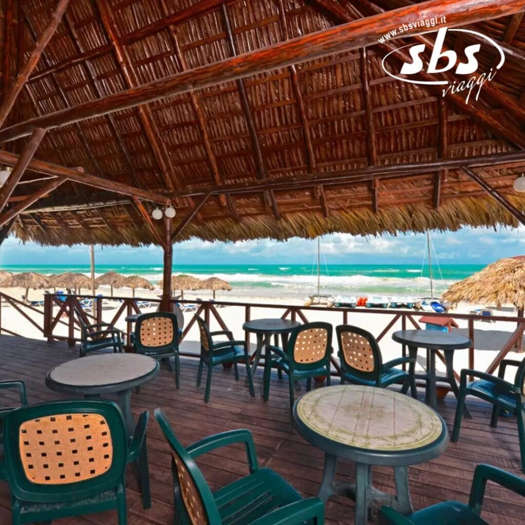 Il bar all'aperto, con tavoli e sedie in legno sotto un tetto di paglia, offre un'atmosfera da