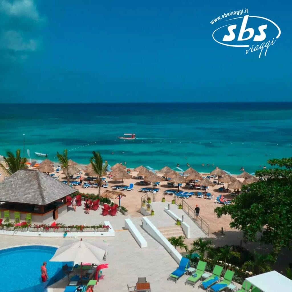 La scena del resort sulla spiaggia Bozza Automatica mostra lettini e ombrelloni a bordo piscina con vista sull'oceano turchese, con i loghi discretamente visibili in alto a destra.