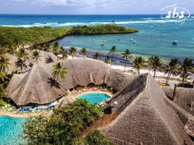Un resort tropicale con strutture dal tetto di paglia, una piscina e palme si affaccia sull'oceano. Nelle vicinanze, le barche sono ormeggiate vicino alla riva sotto lo sguardo sereno di una piccola isola sullo sfondo, una bozza automatica senza soluzione di continuità del paradiso.